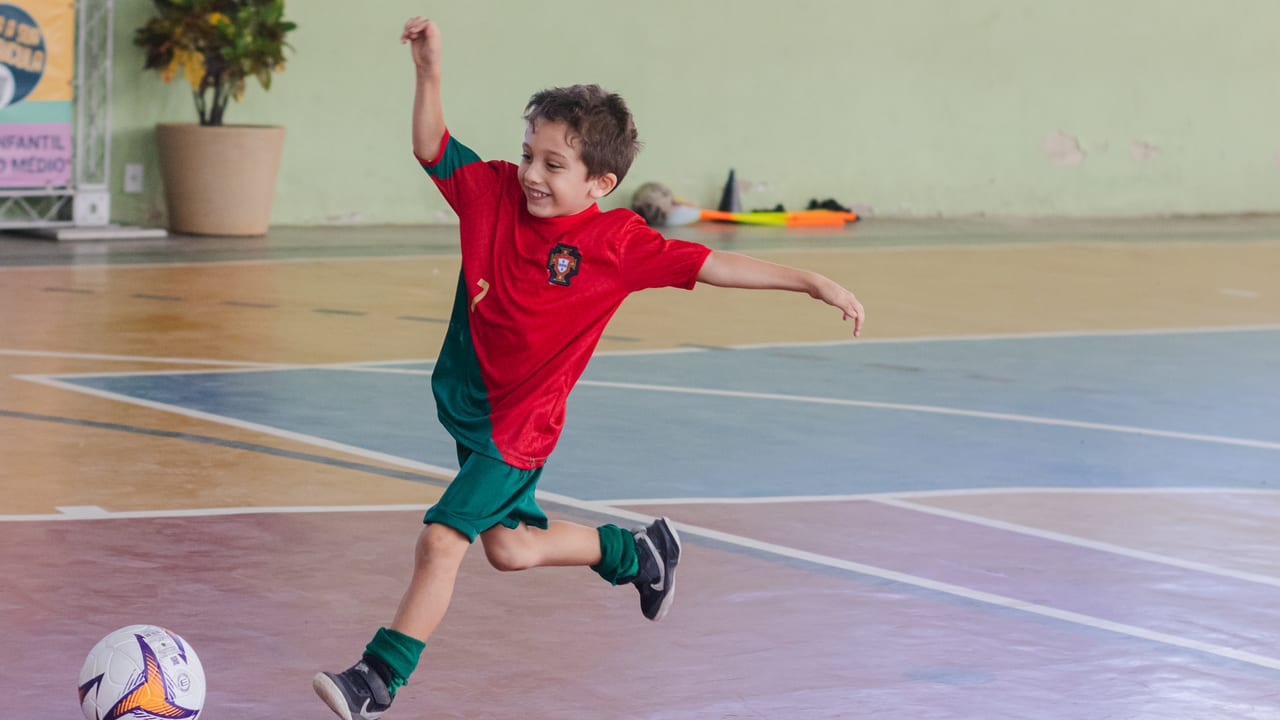 Aluno chutando a bola durante aula de futebol na quadra